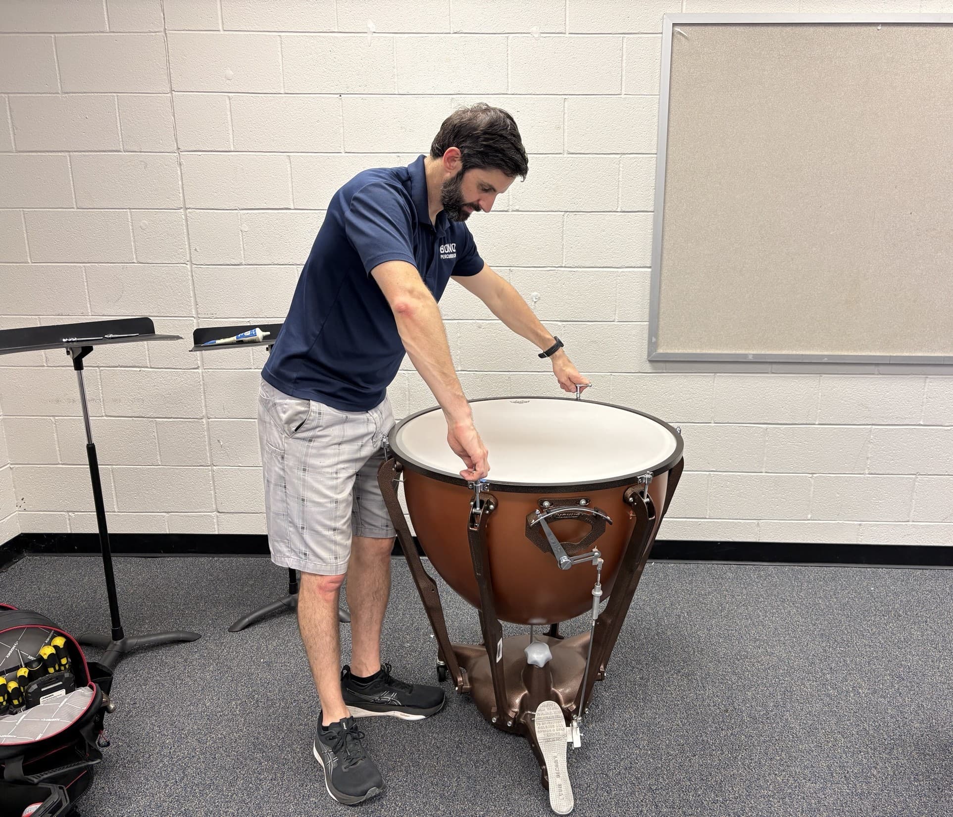 A Bono Percussion technician tensioning a timpani head in a school band room