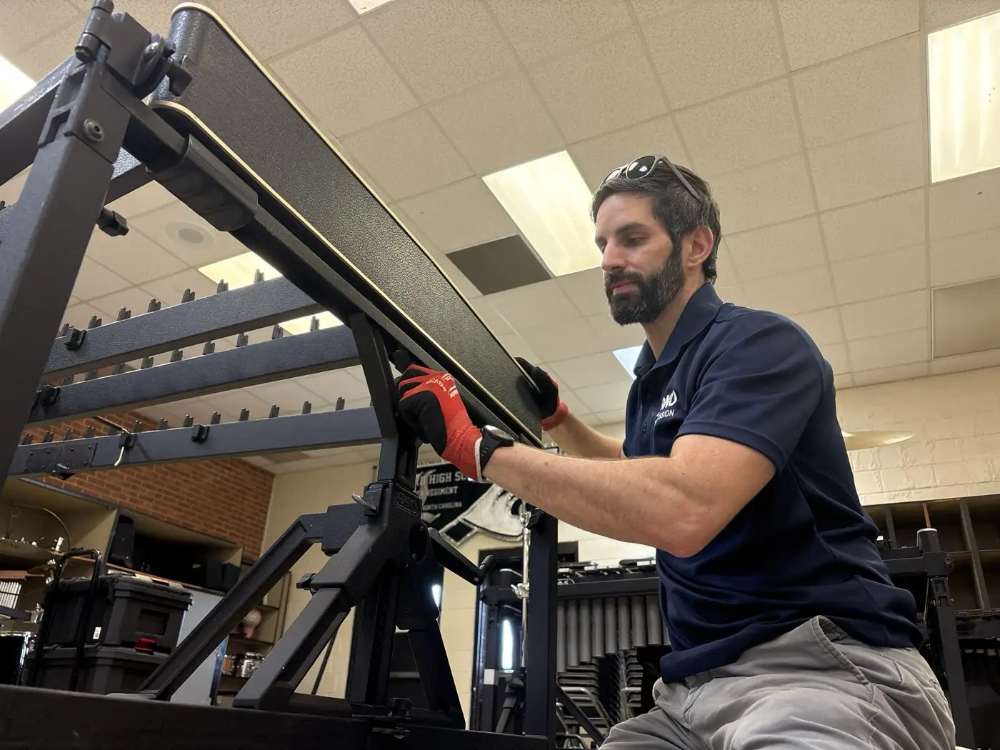 A Bono Percussion technician checking a marimba frame hinge and rail alignment on site at a high school band room