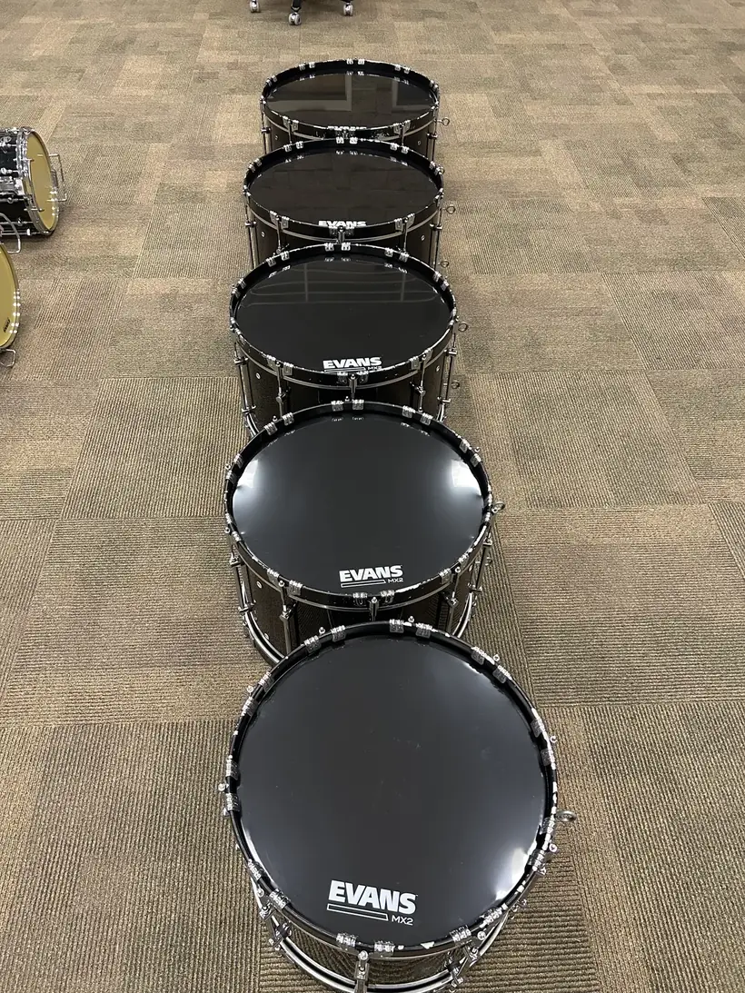 A line of marching bass drums with fresh black heads installed, ready to tune