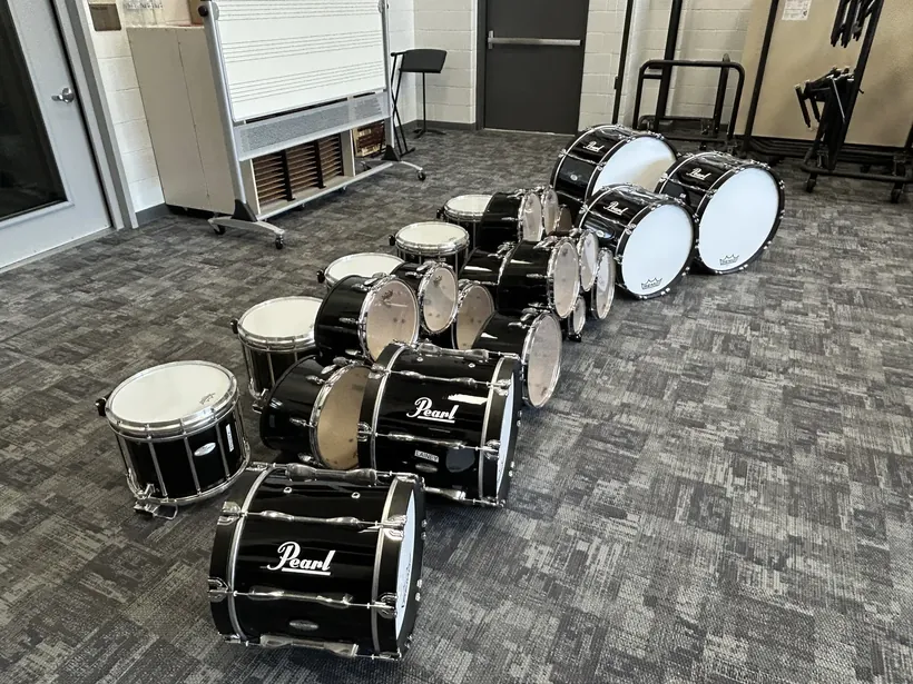 A complete Pearl drumline set laid out on the floor: marching snares, tenors, and bass drums